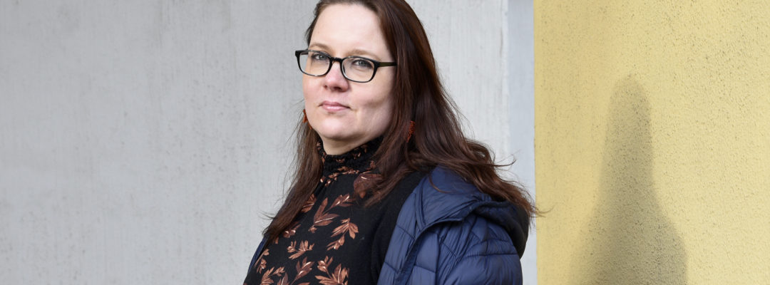 FinFamin Työ tukee -kampanjan kuva_Nainen seisoo harmaan taustan edessä